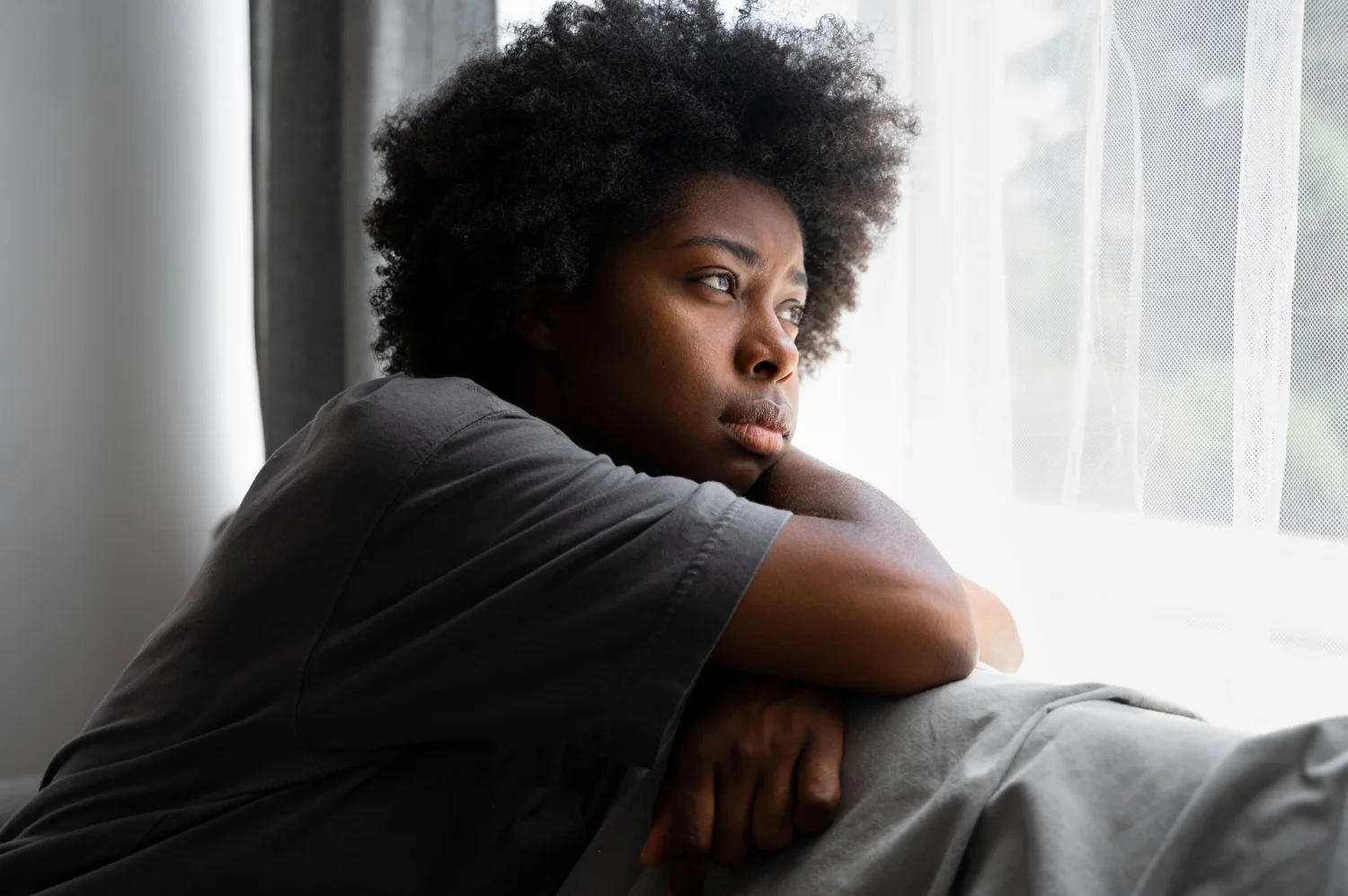 Une femme regarde par la fenêtre, les bras appuyés sur un coussin.